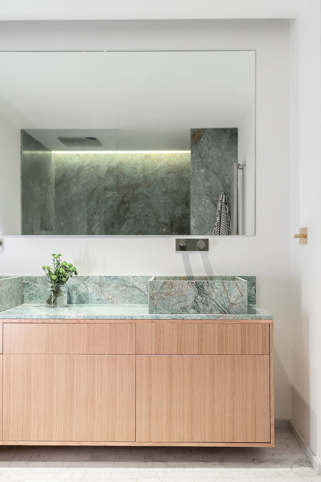 A modern bathroom with a green marble sink and vanity, subtle lighting, and a large mirror.