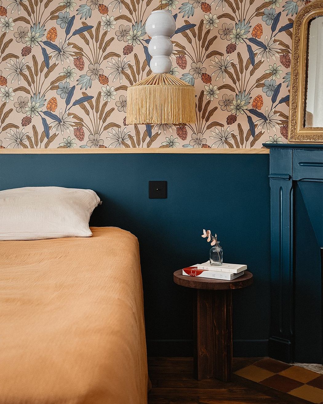 Vibrant floral wallpaper, rattan lighting, and rich, dark accents create a cozy, stylish bedroom.