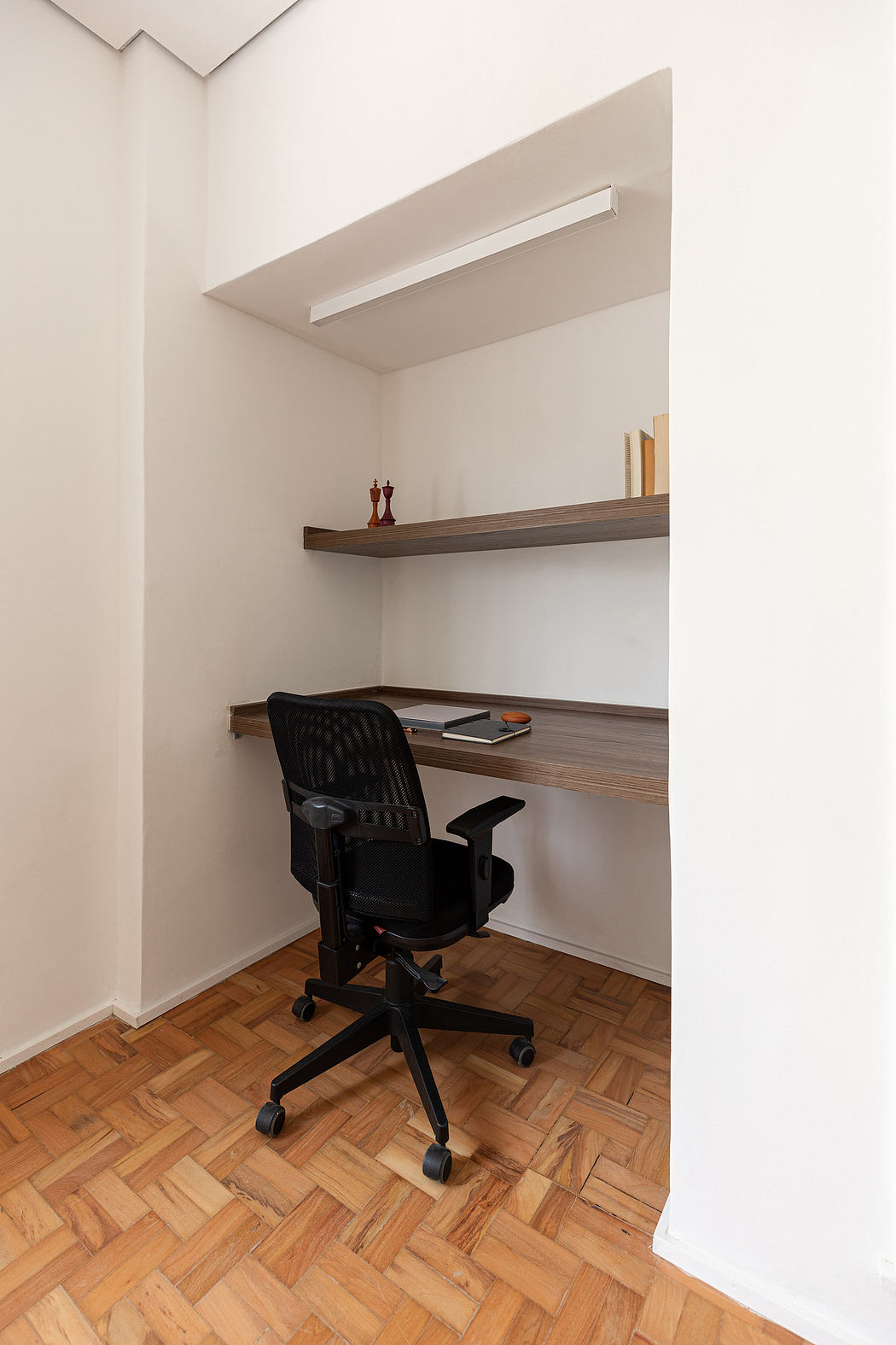 Minimalist home office nook with wooden floating shelves and a black office chair.