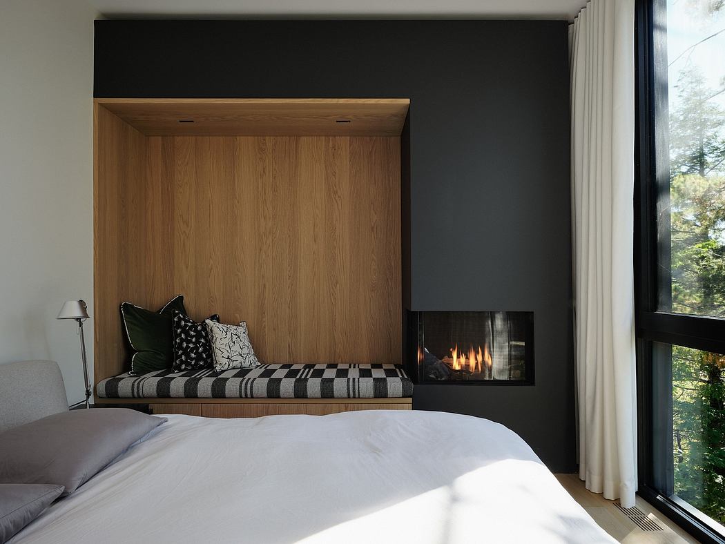 Cozy bedroom with wooden built-in, fireplace, and expansive window framing the outdoors.