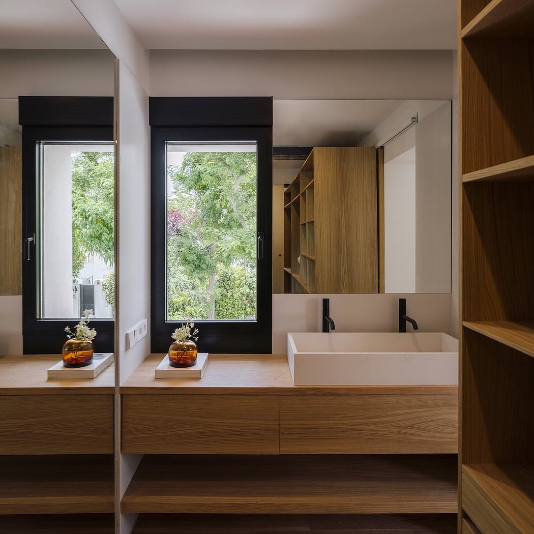 Minimalist bathroom with sleek wooden vanity, angular vessel sinks, and large windows overlooking lush greenery.
