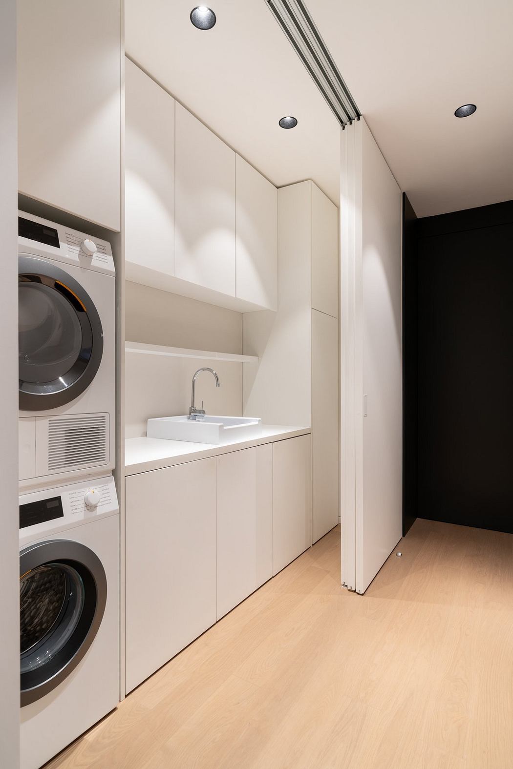 A modern, minimalist laundry room with integrated appliances and a sleek, white cabinetry design.