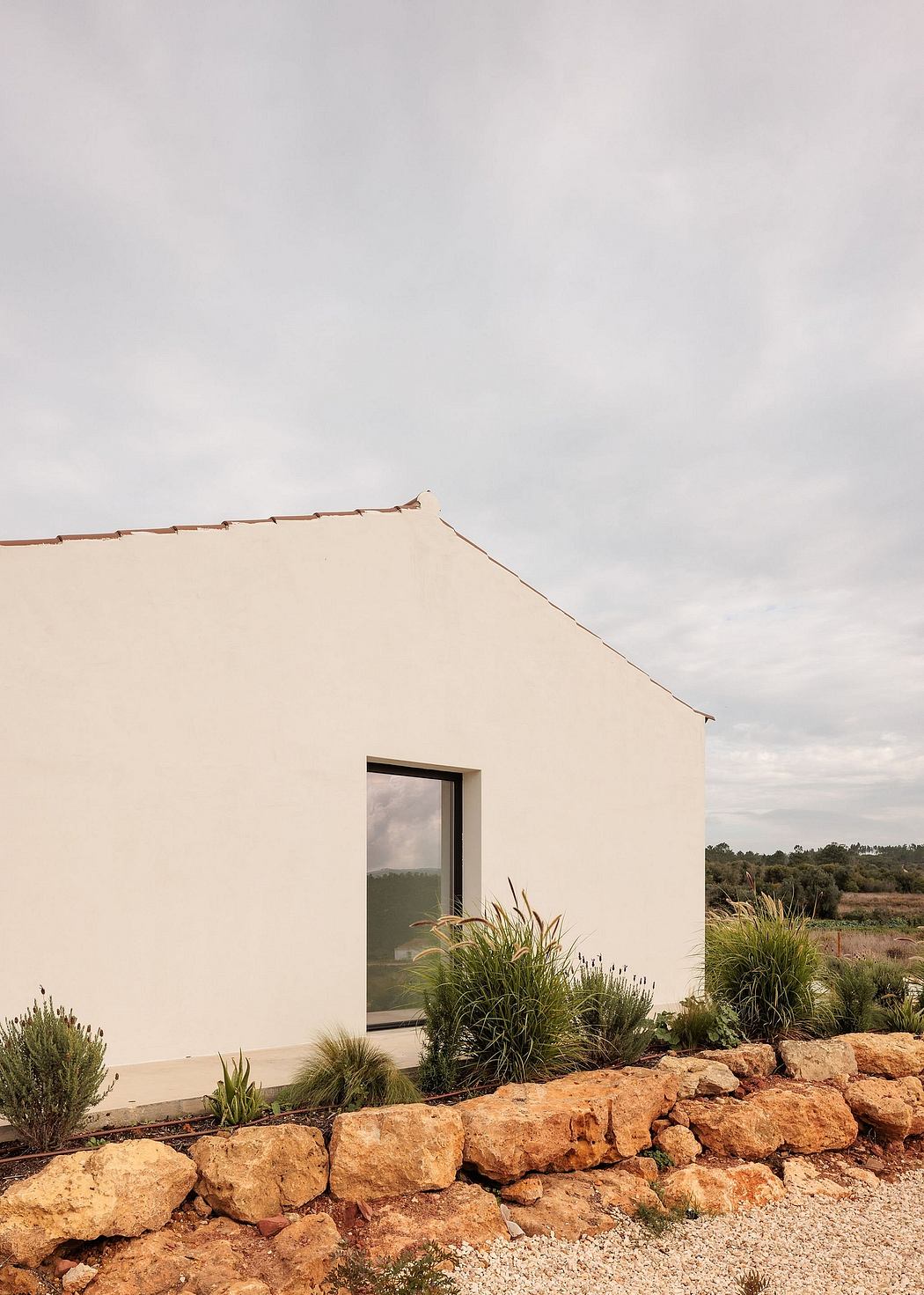 A modern, minimalist building with a stone retaining wall and lush native vegetation.