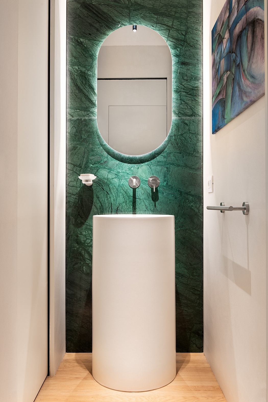 Stylish bathroom with striking green marble walls, circular mirror, and contemporary pedestal sink.