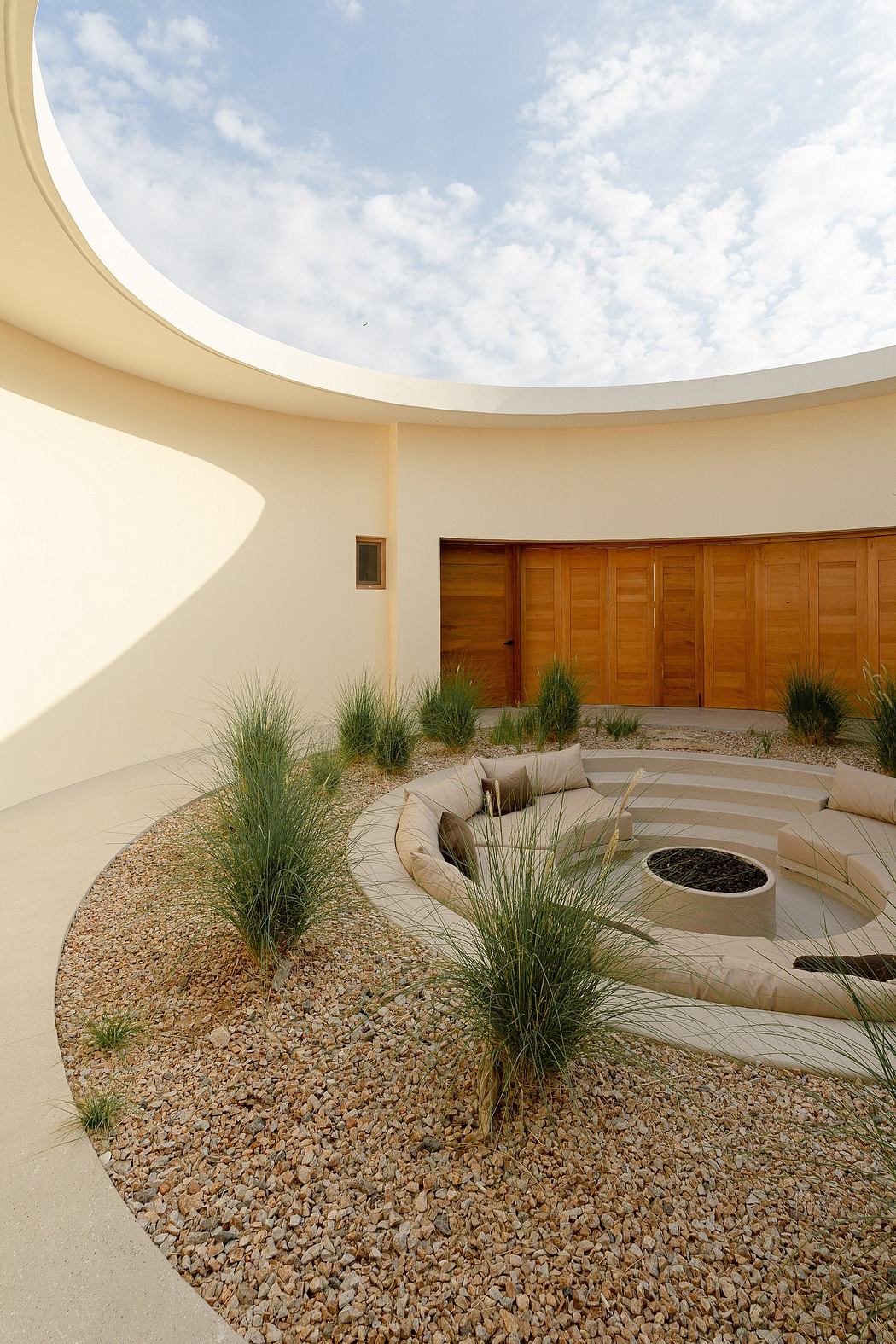 Architecturally striking outdoor space with circular design, wood doors, and decorative grasses.