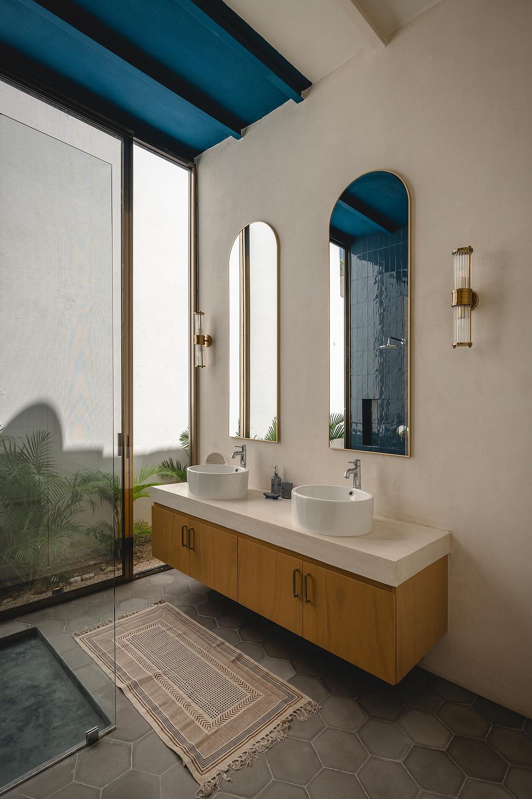 Sleek, minimalist bathroom with wooden vanity, arched mirrors, and vibrant blue ceiling.