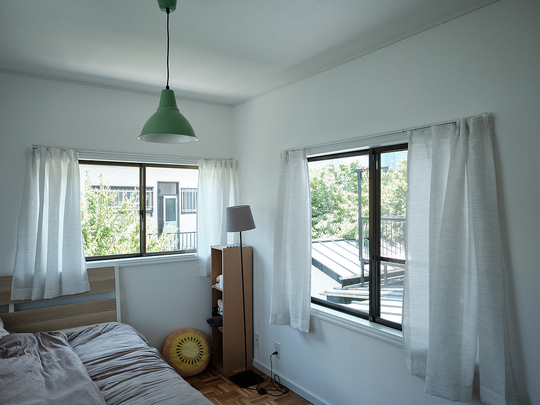 Minimalist bedroom with green pendant light, large windows, and wooden floor. Cozy and bright space.