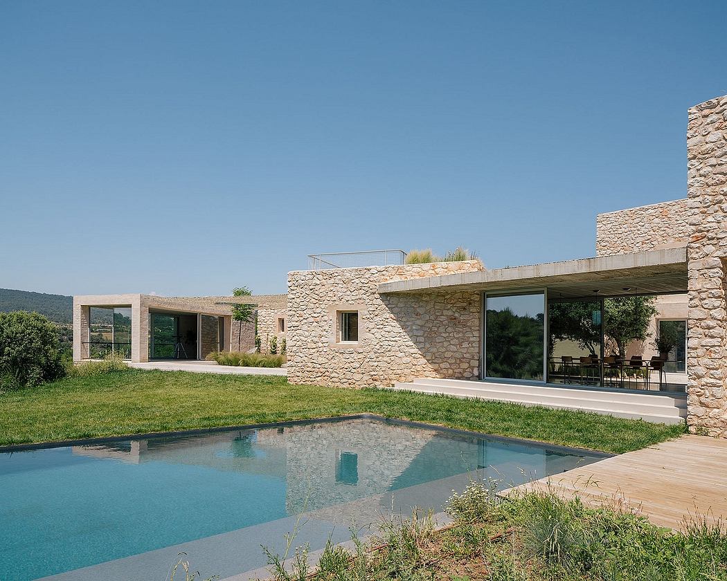 A modern stone villa with glass walls, a pool, and lush landscaping.