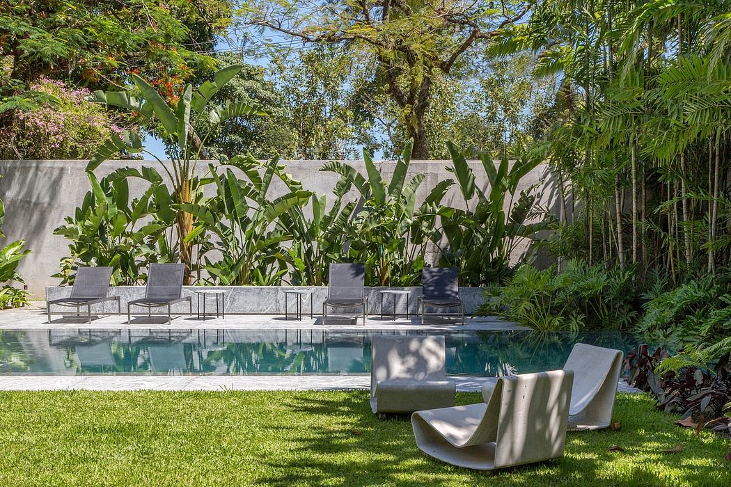A lush tropical garden surrounds a serene swimming pool with modern poolside furniture.