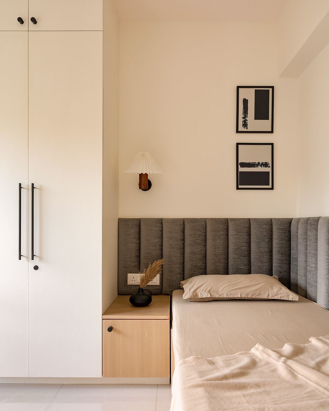 A minimalist bedroom with a gray upholstered headboard, wooden nightstand, and framed artwork.