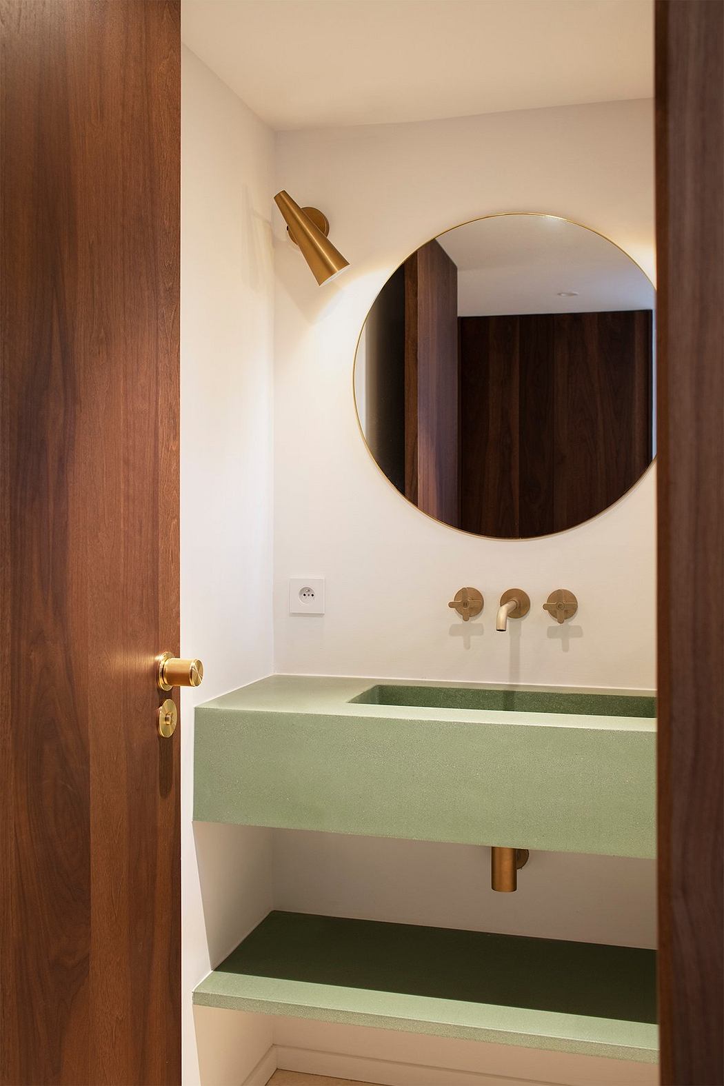 Minimalist bathroom design featuring green stone vanity, round mirror, and brass fixtures.