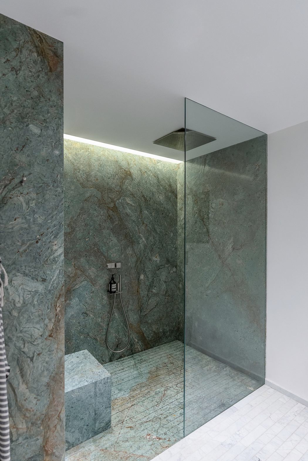 A modern, minimalist bathroom with floor-to-ceiling glass walls and a marble-clad shower.