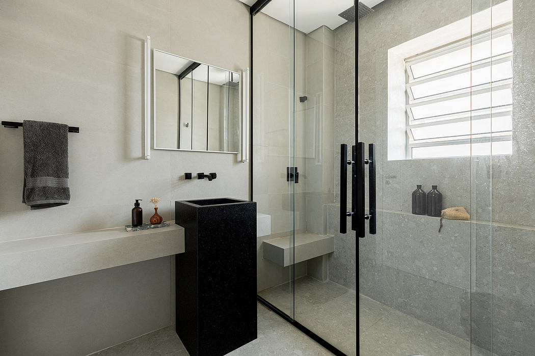 A modern bathroom with gray tile walls, a black vanity, and a glass shower enclosure.