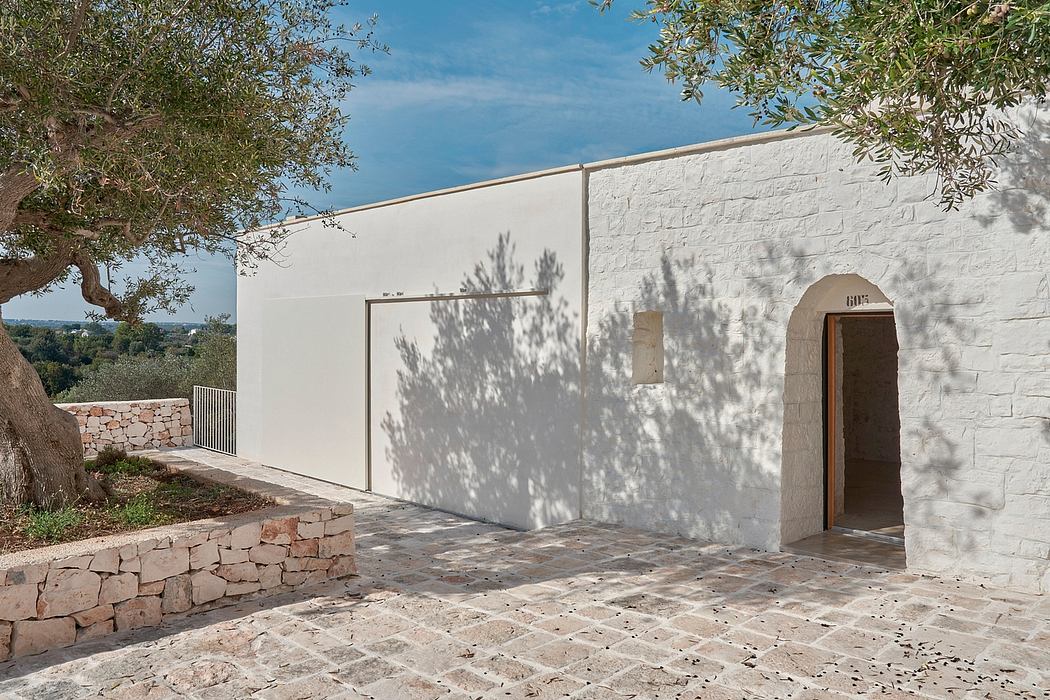 A minimalist Mediterranean-style building with clean white walls, arched doorway, and stone paved patio.