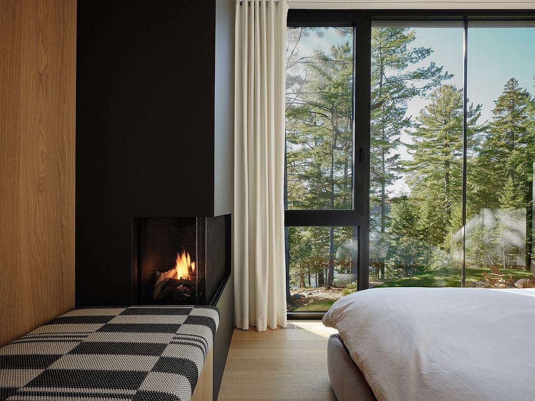 Cozy bedroom with a fireplace, large windows, and a view of the scenic forest.