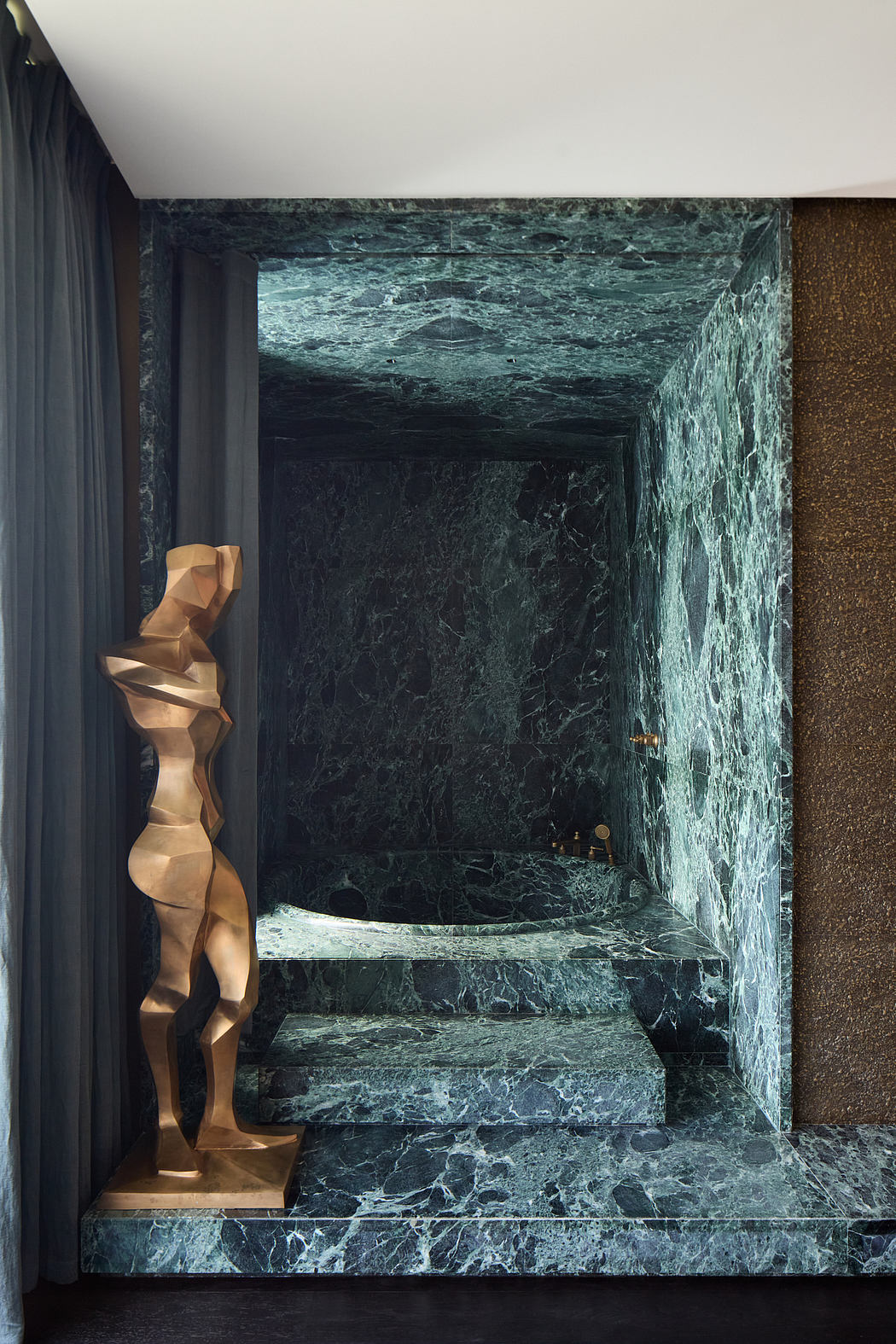 Sleek, modern bathroom with dramatic green marble walls and a sculptural golden accent.