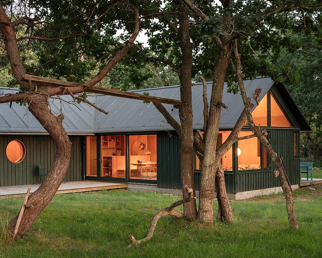 A modern a-frame cabin with floor-to-ceiling windows, nestled among mature trees on a grassy lawn.