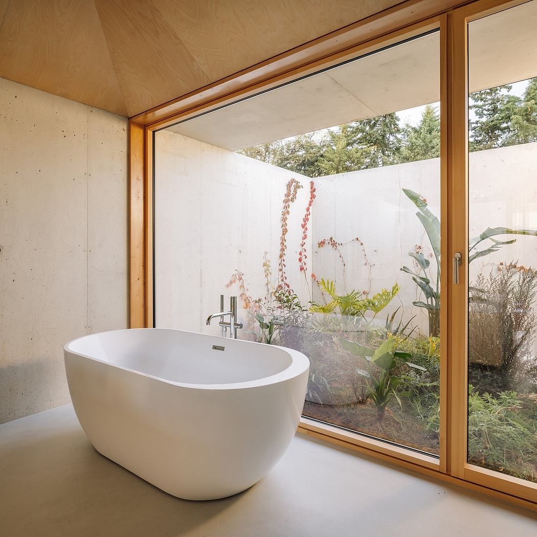 Modern bathroom with a freestanding bathtub and expansive glass windows overlooking a lush forest landscape.