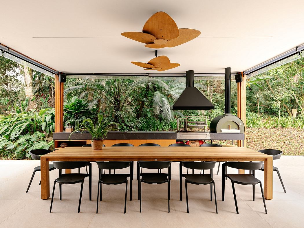 A modern, open-air dining area surrounded by lush greenery and featuring a wooden table, black chairs, and a unique fan-shaped light fixture.