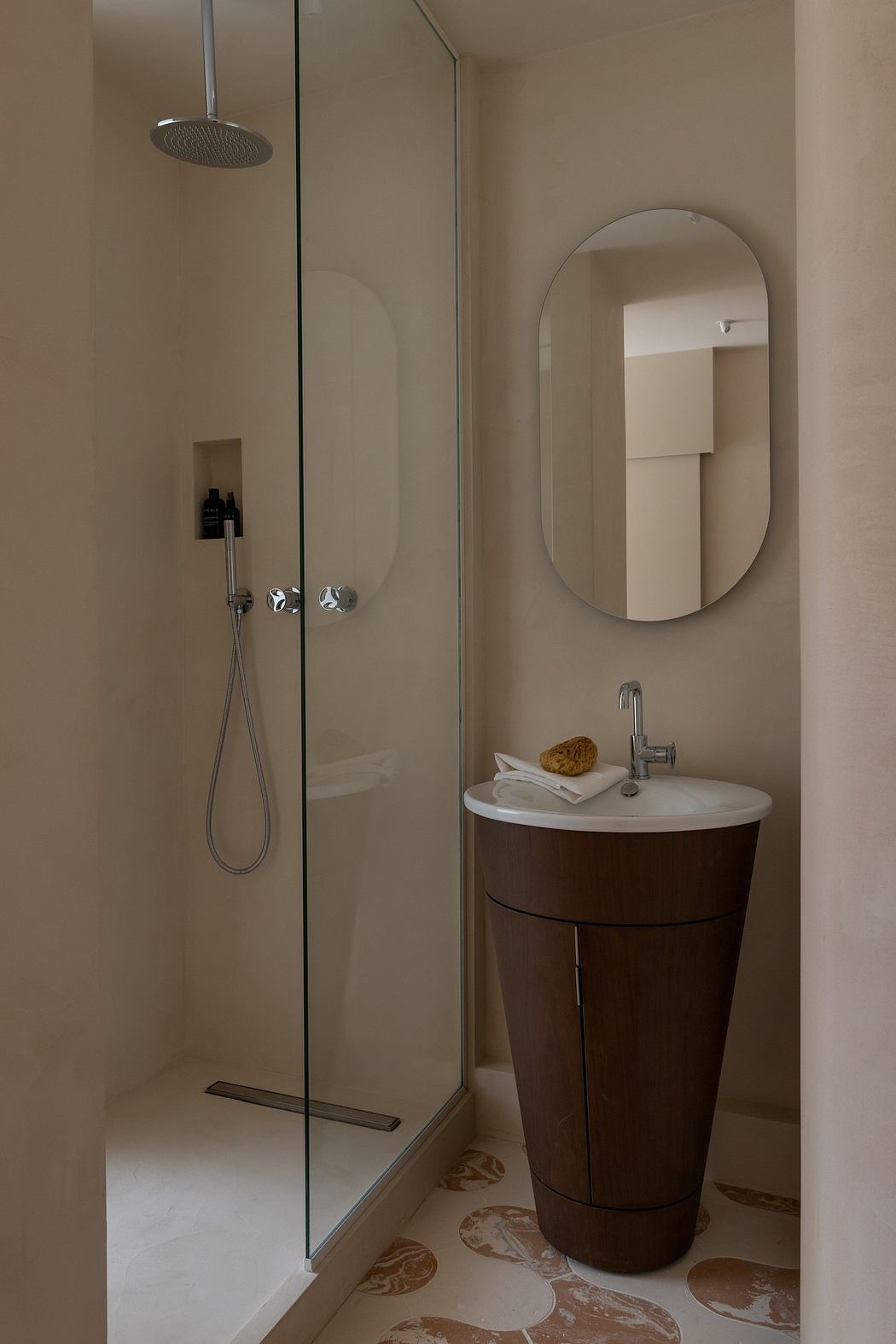 Minimalist bathroom with glass shower, rounded vanity, and patterned floor tiles.