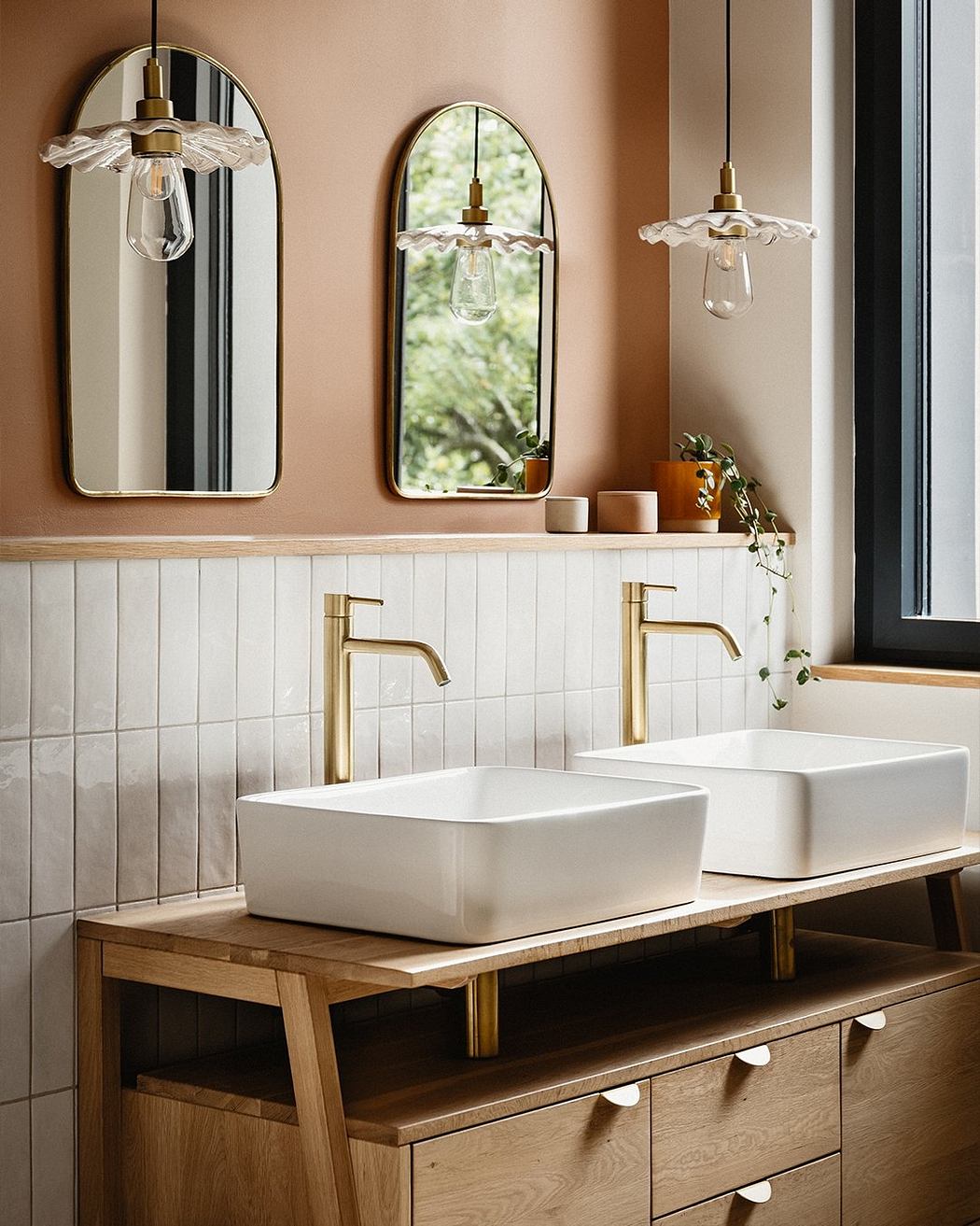 Elegant bathroom with white vessel sinks, gold faucets, arched mirrors, and pendant lights.