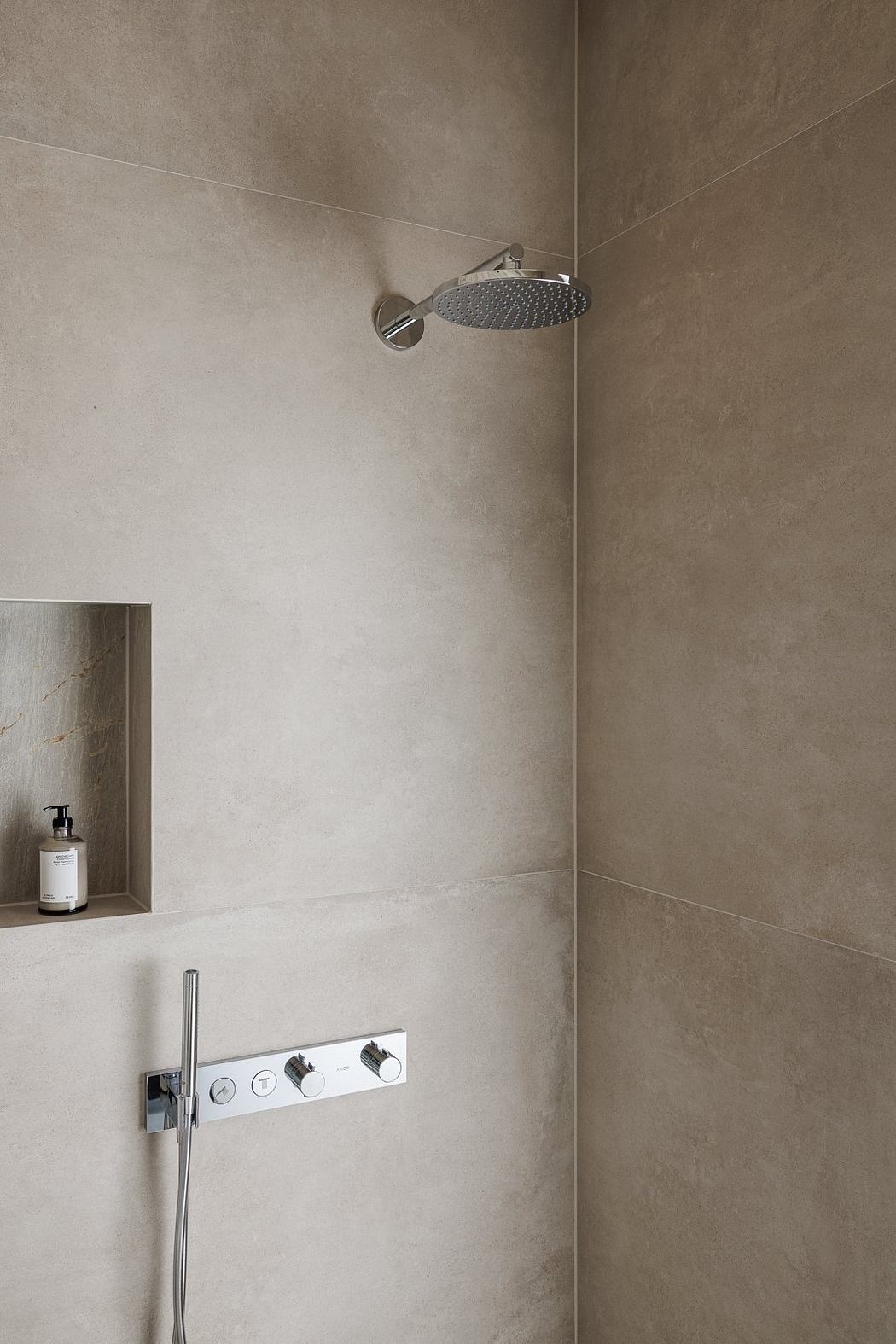 A minimalist shower with a circular showerhead and built-in soap niche.