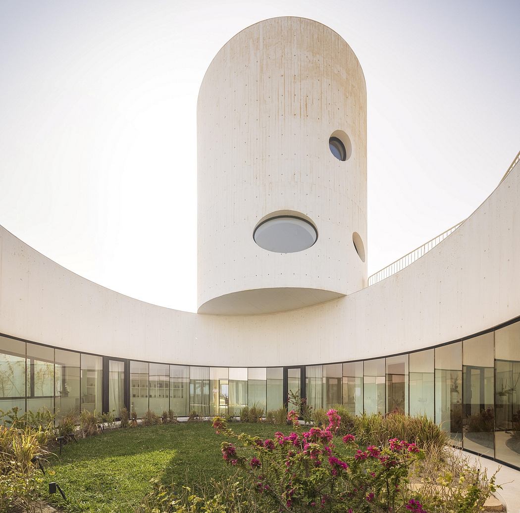 The image depicts a circular architecture with a tall, cylindrical structure and a lush, landscaped interior courtyard.