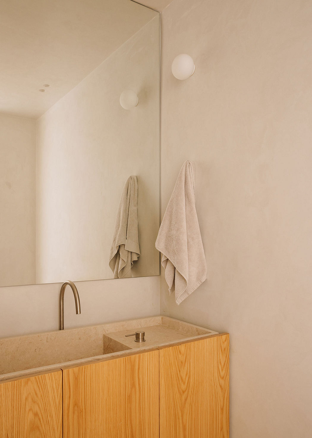 A minimalist bathroom with a wood vanity, stone sink, and recessed lighting fixtures.