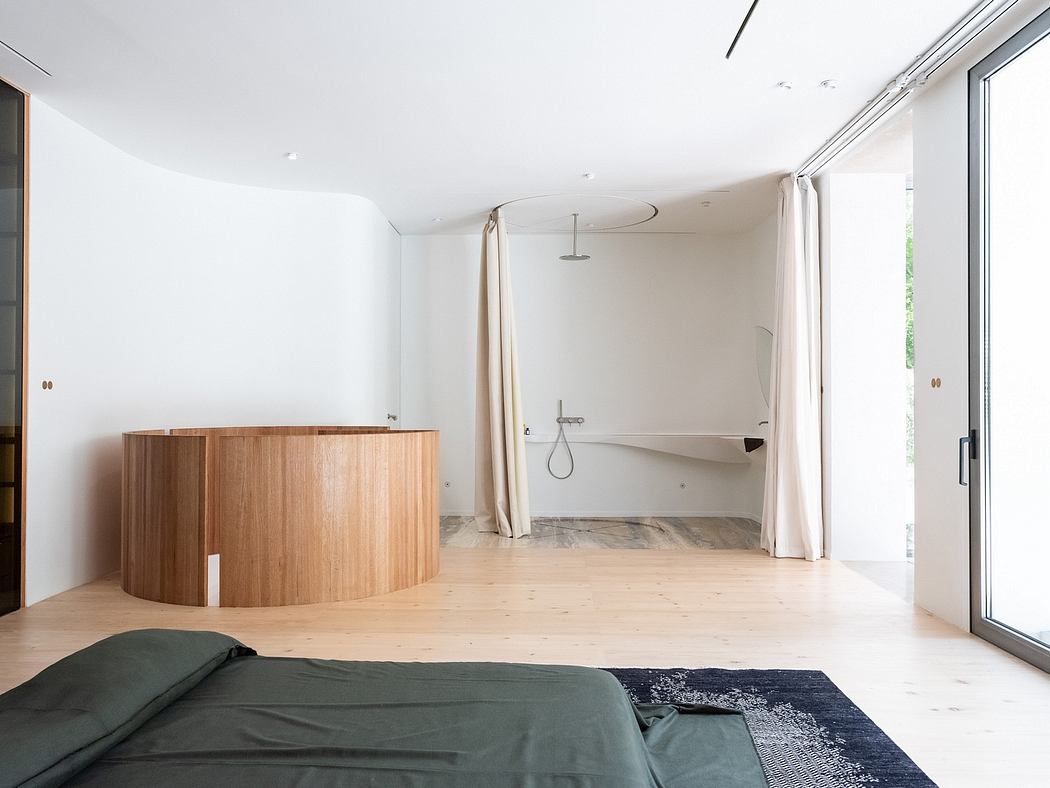 Spacious, minimalist bedroom with curved wood furnishings, large windows, and ensuite bathroom.