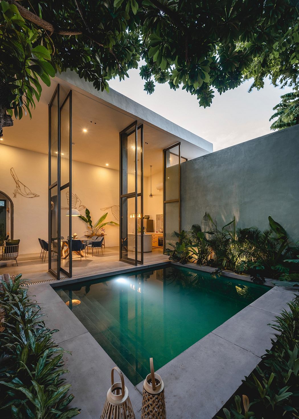 Striking modern architecture with a tranquil pool, lush tropical foliage, and cozy furnishings.