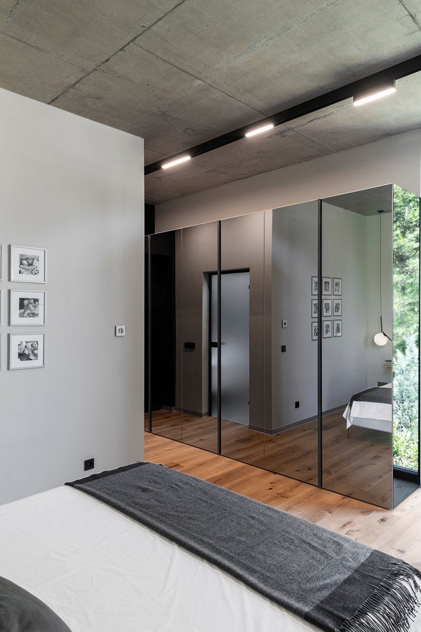 Minimal, modern bedroom with concrete ceiling, mirrored closet, and wood flooring.