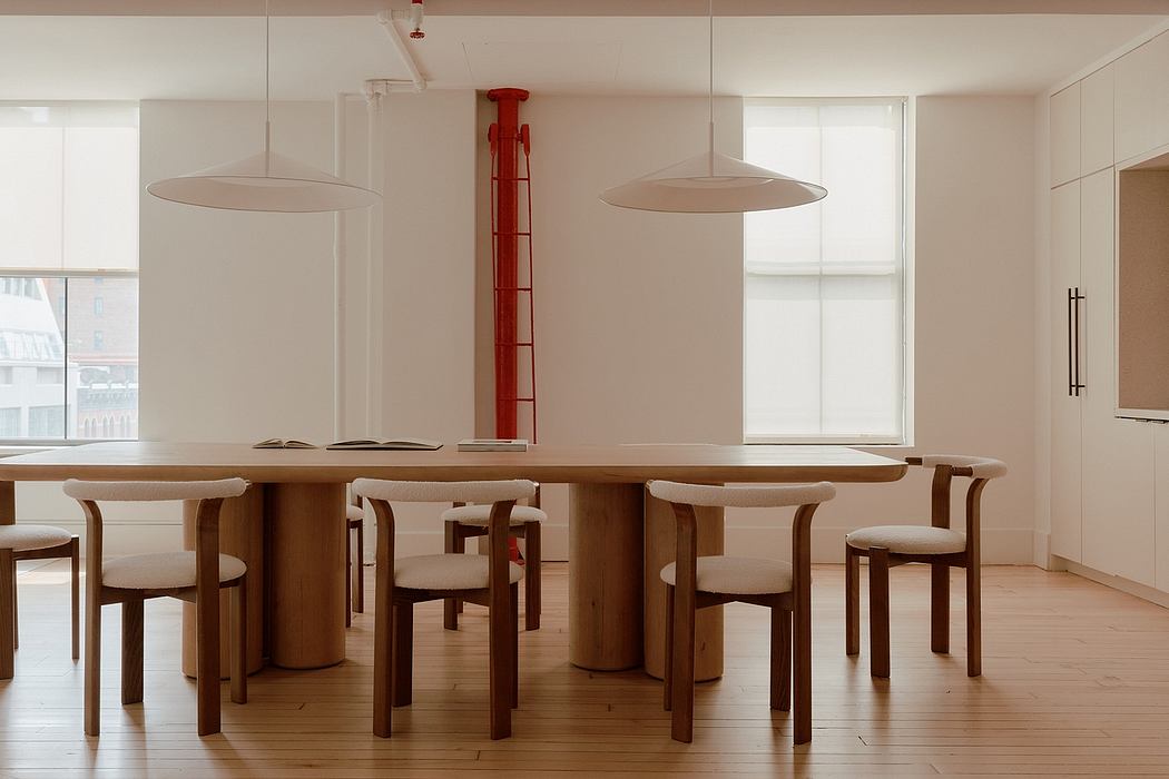 Minimalist dining space with wooden table, chairs, and distinctive red column lamp.