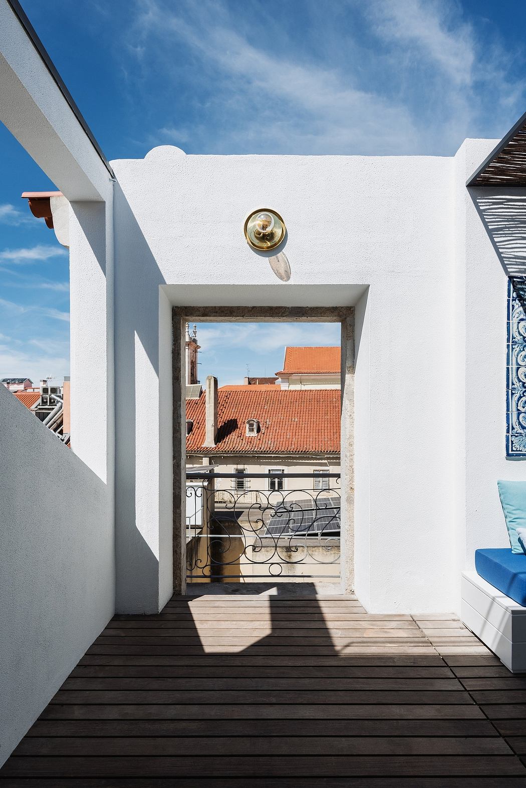 A white, minimalist balcony with a metal railing overlooking a traditional rooftop.