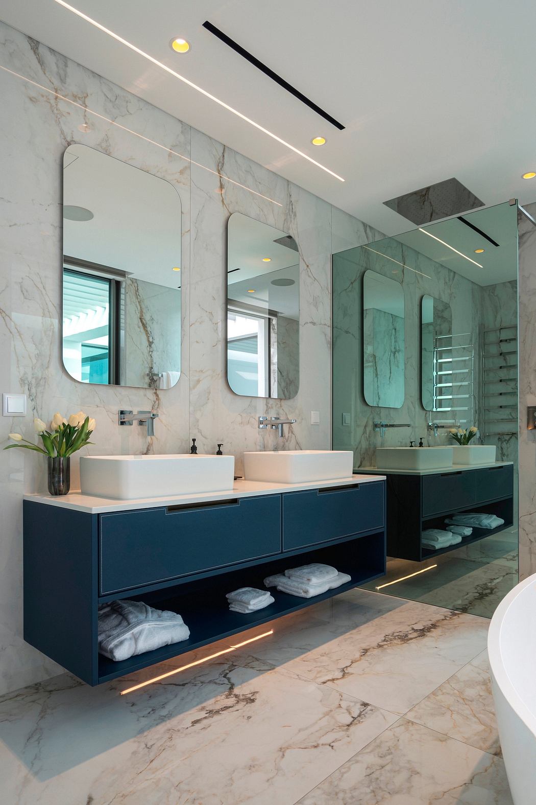 A modern bathroom with marble walls, recessed lighting, and floating vanity cabinets.