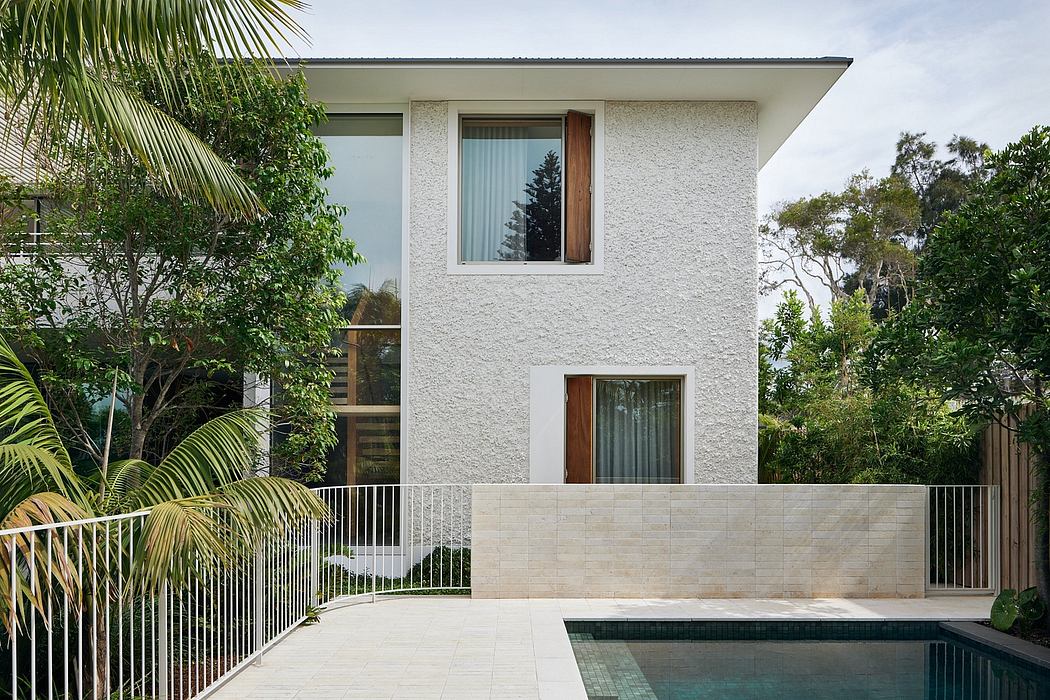 Modern white stucco house with large windows, concrete patio, and swimming pool surrounded by lush greenery.
