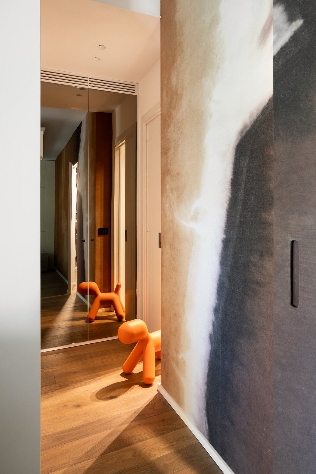 A narrow hallway with a dark-colored textured wall, wooden flooring, and two orange sculptural objects.