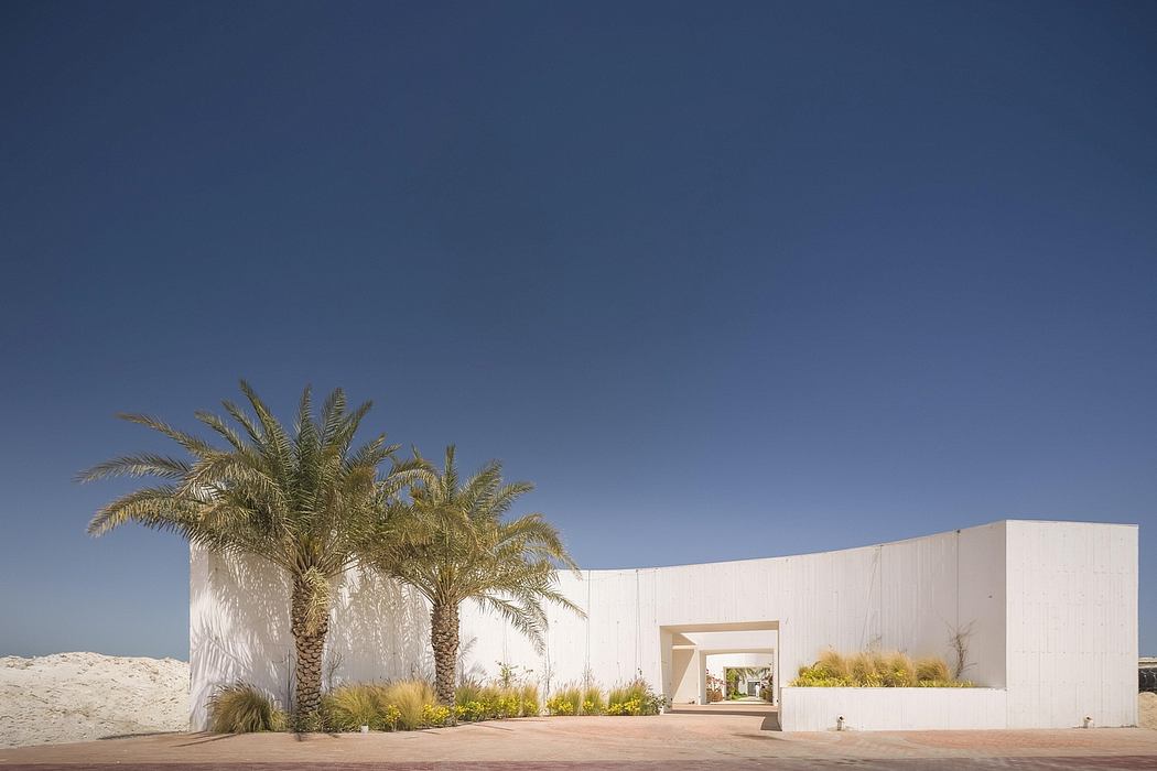 A modern, minimalist building with palm trees framing the entrance against a clear blue sky.