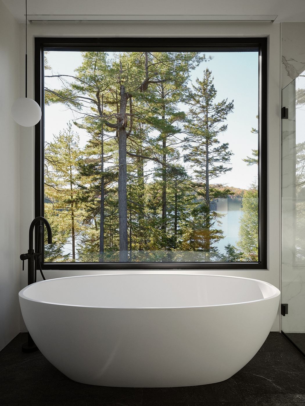 Minimalist bathroom with a freestanding oval tub, framed by a large window overlooking a serene forest landscape.