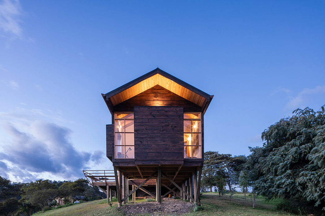 A rustic wooden cabin elevated on stilts, featuring a pitched roof and illuminated windows.