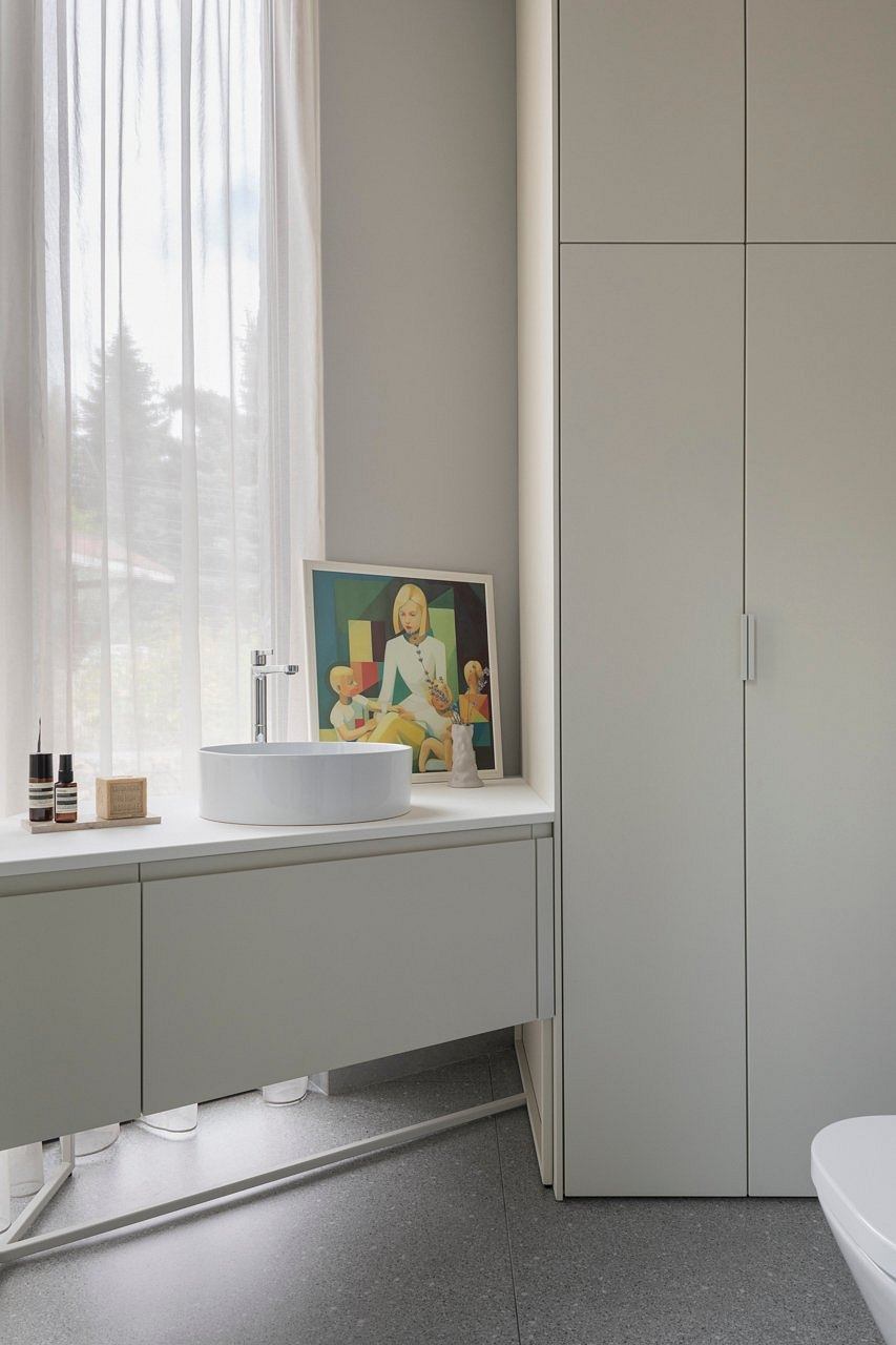 Minimalist bathroom with white vanity, colorful artwork, and sleek cabinet doors.