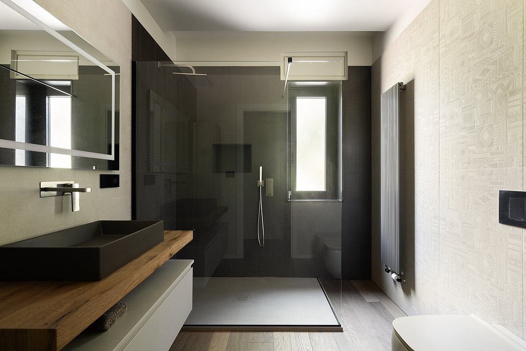 Modern bathroom with dark tiles, wooden vanity, and glass shower enclosure.