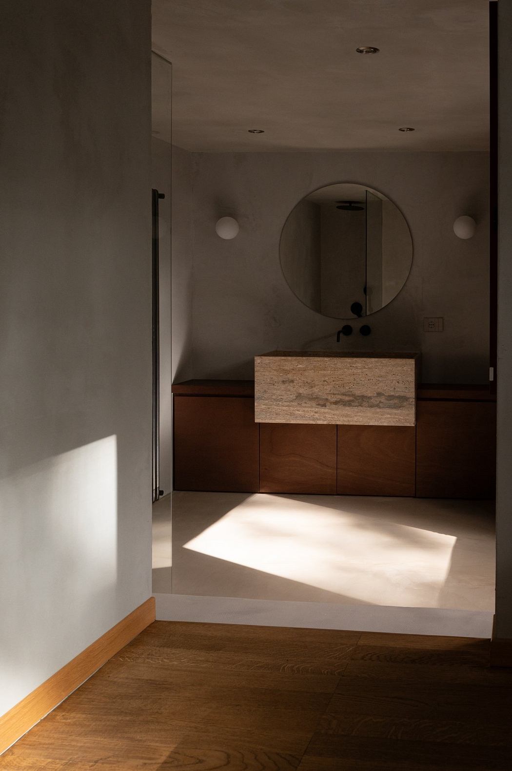 A modern bathroom with a round mirror, wooden vanity, and neutral tones. Sleek and minimalist design.