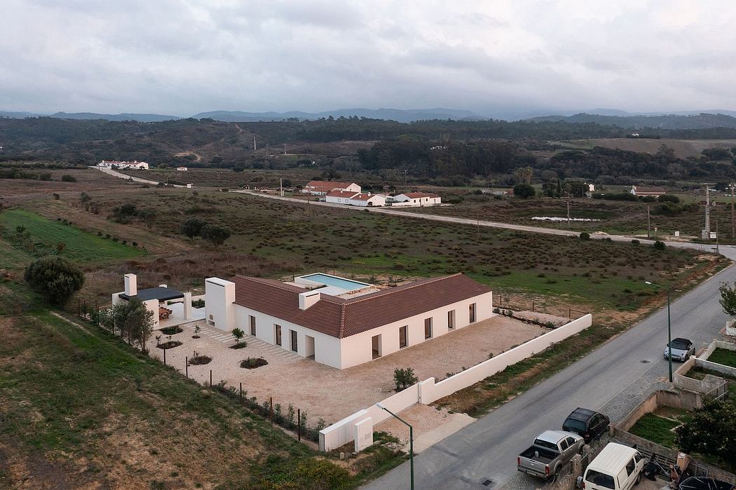 A modern white building with a red tile roof and a pool, set against a hilly, rural landscape.