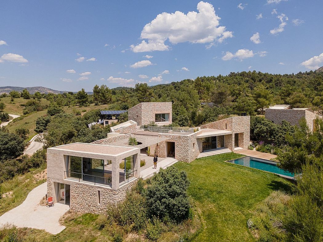 A contemporary villa with stone walls, a pool, and a lush green landscape.