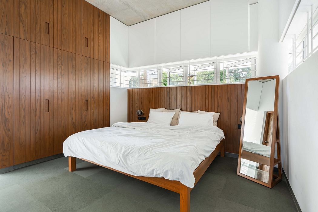 Cozy bedroom with wooden paneling, high ceilings, and large windows overlooking trees.