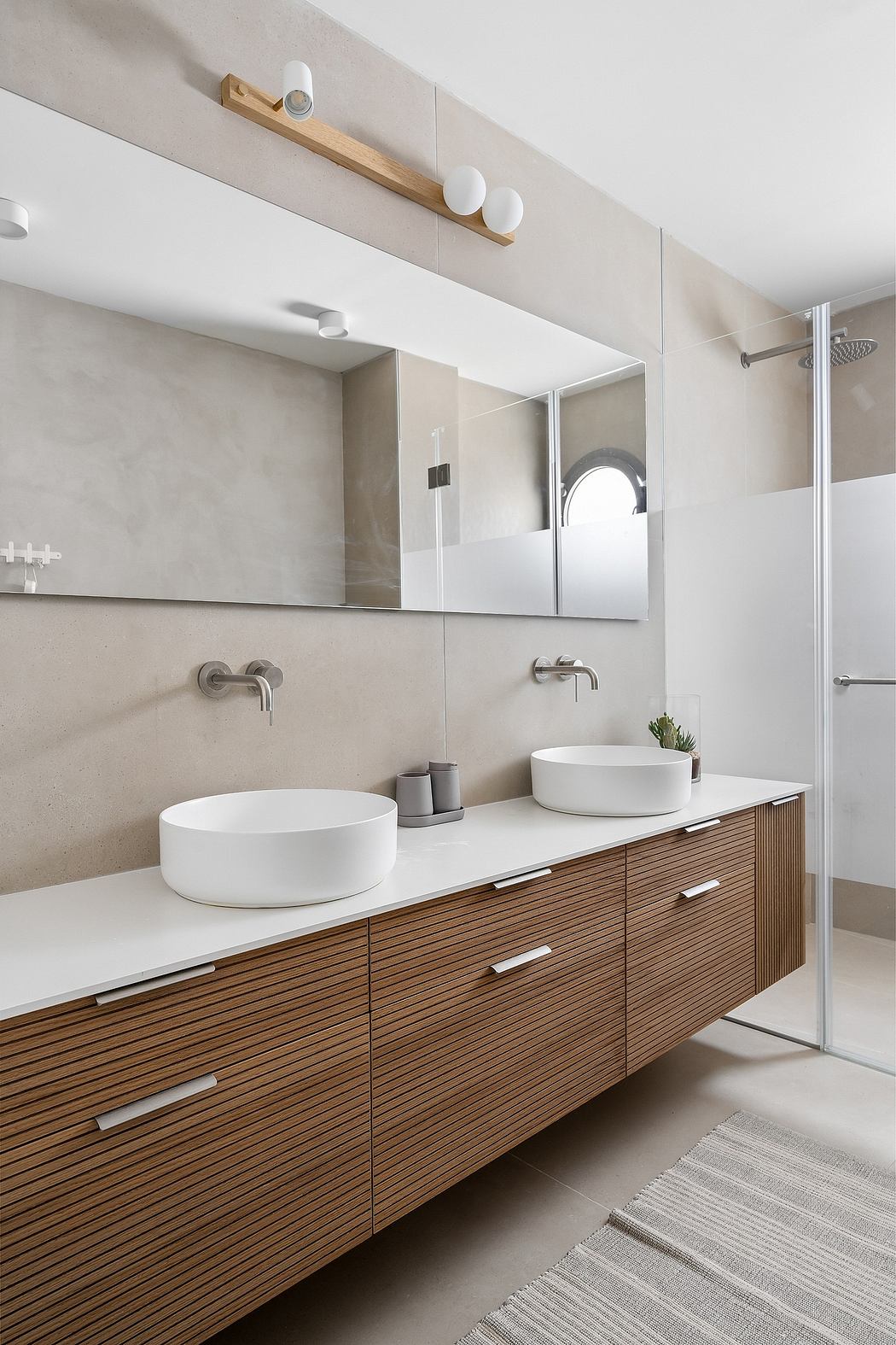 A modern, minimalist bathroom with a wooden vanity, vessel sinks, and a mirror wall.