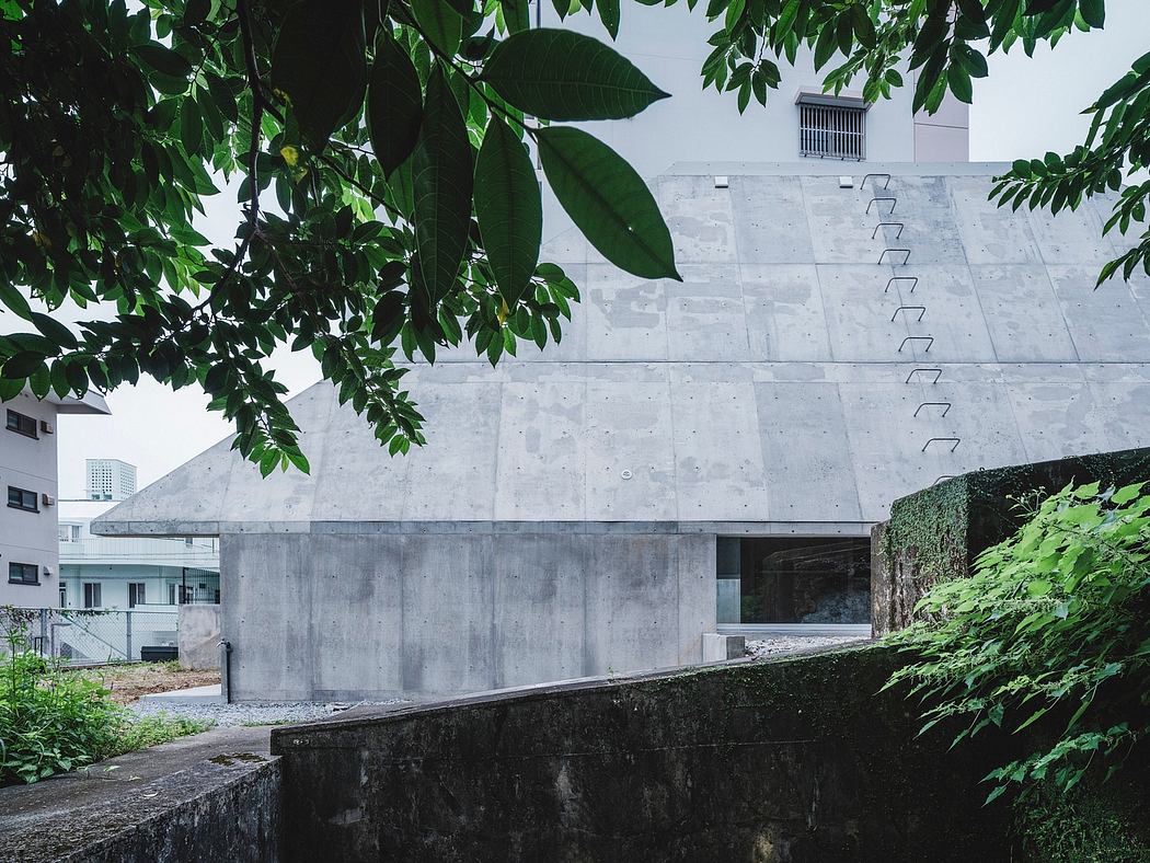 A modern concrete structure with unique geometric patterns, framed by lush foliage.