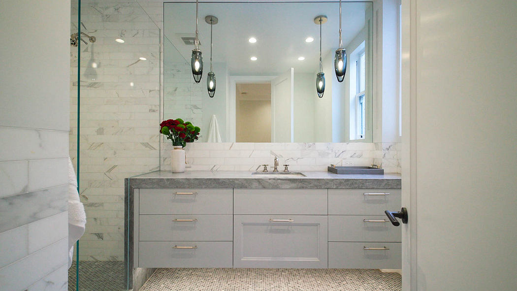 A modern, marble-clad bathroom with sleek vanity, pendant lights, and tile flooring.
