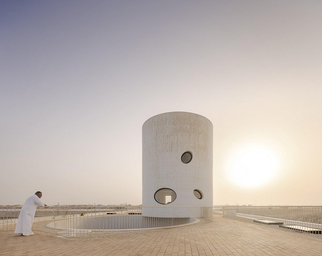 A striking circular concrete structure against a serene sky, with a lone figure.