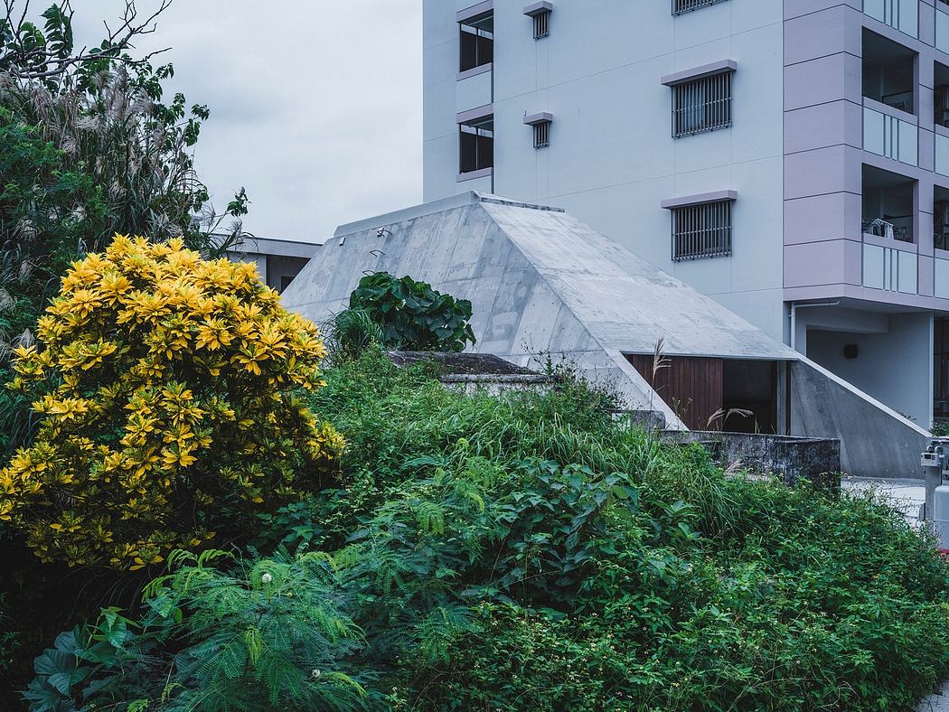 A concrete pyramidal structure surrounded by lush greenery and yellow flowers.